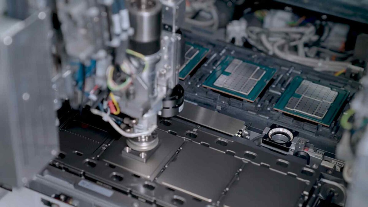 Close-up of a machine assembling electronic components on a circuit board. Wires and various mechanical parts are visible, showcasing a high-tech manufacturing process in progress.