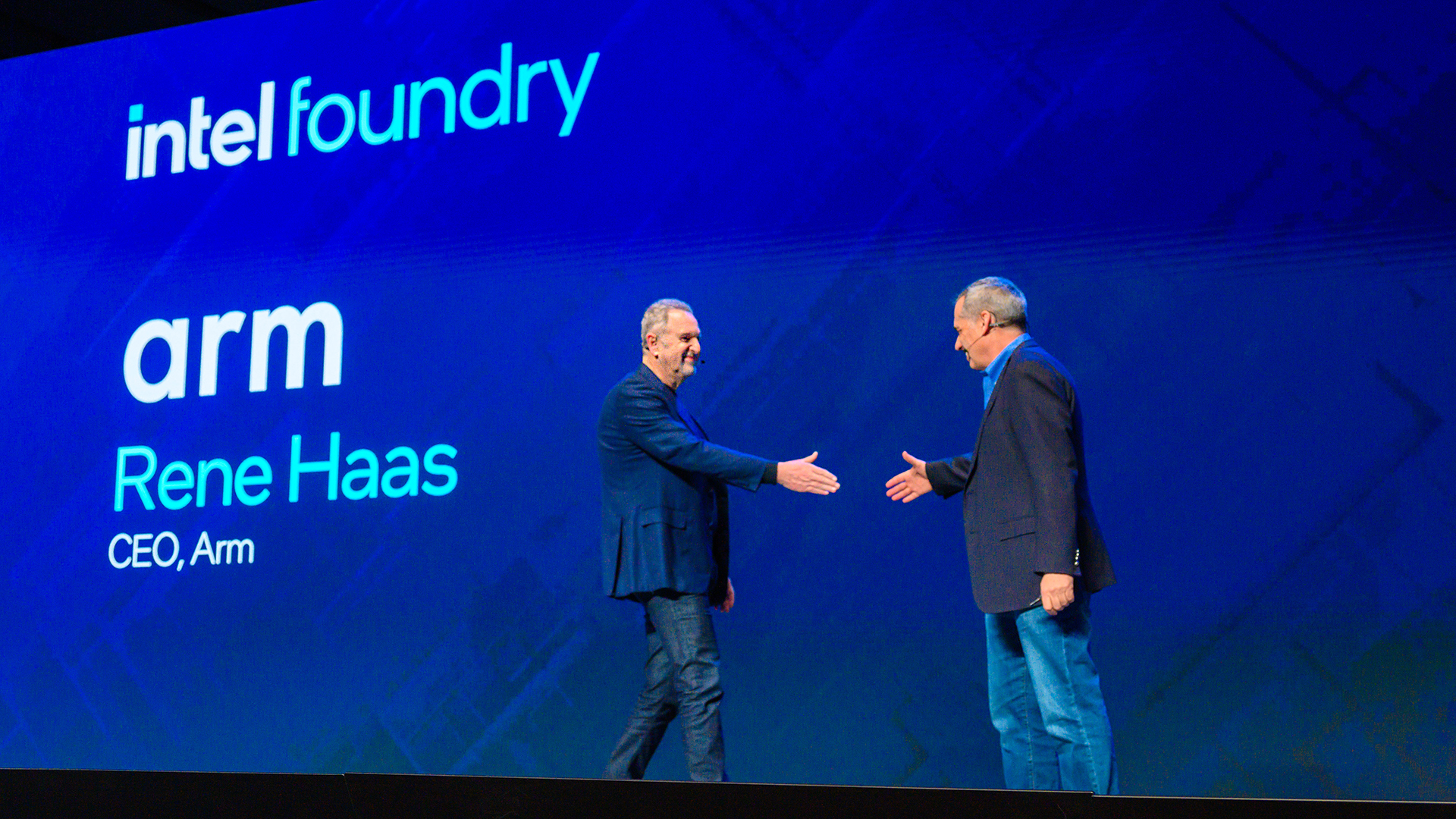 Two men shaking hands on stage in front of a large screen displaying the logos for Intel Foundry and ARM, with the text Rene Haas, CEO, Arm.