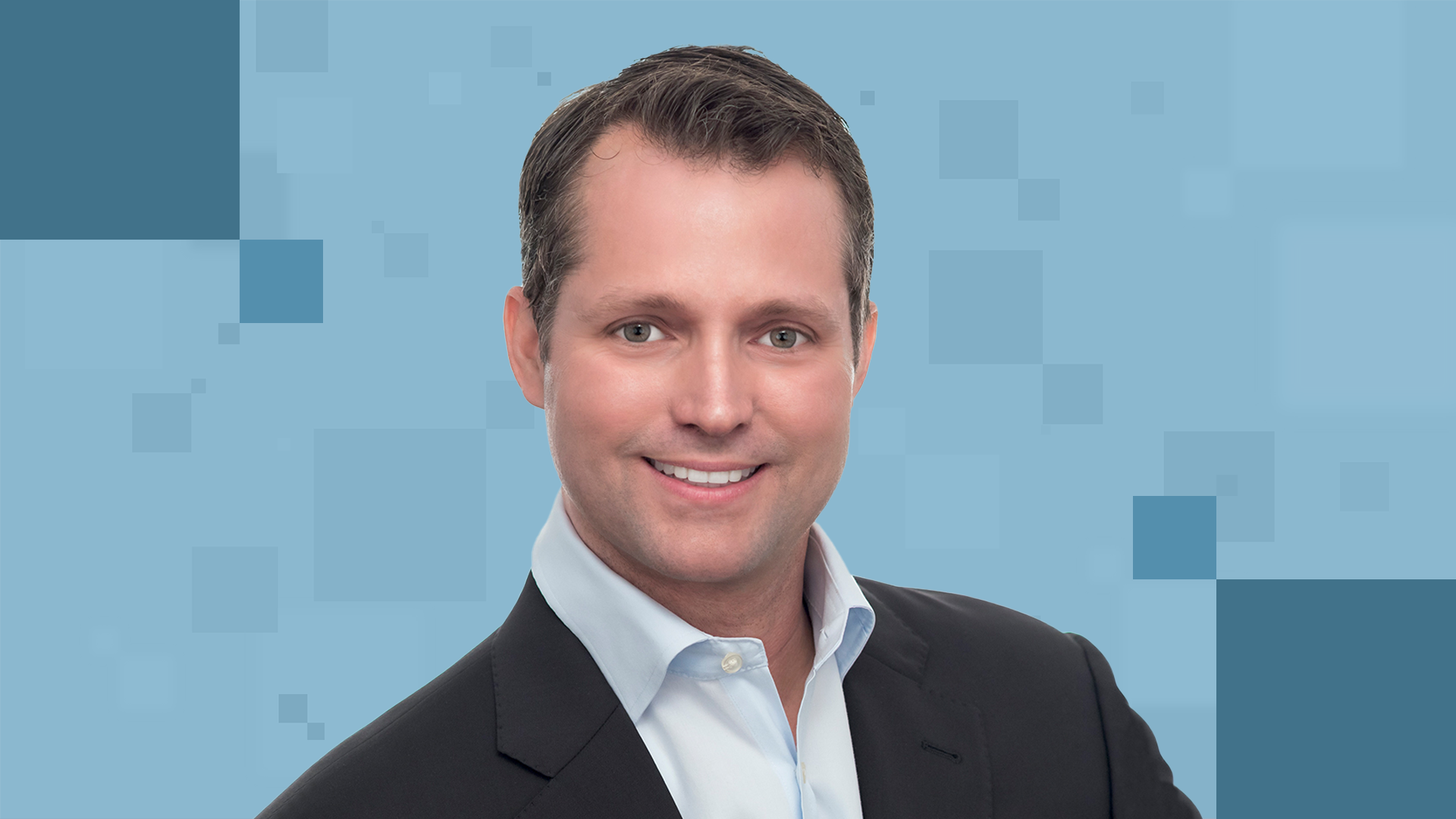 A man in a suit smiles at the camera against a blue background with geometric patterns.