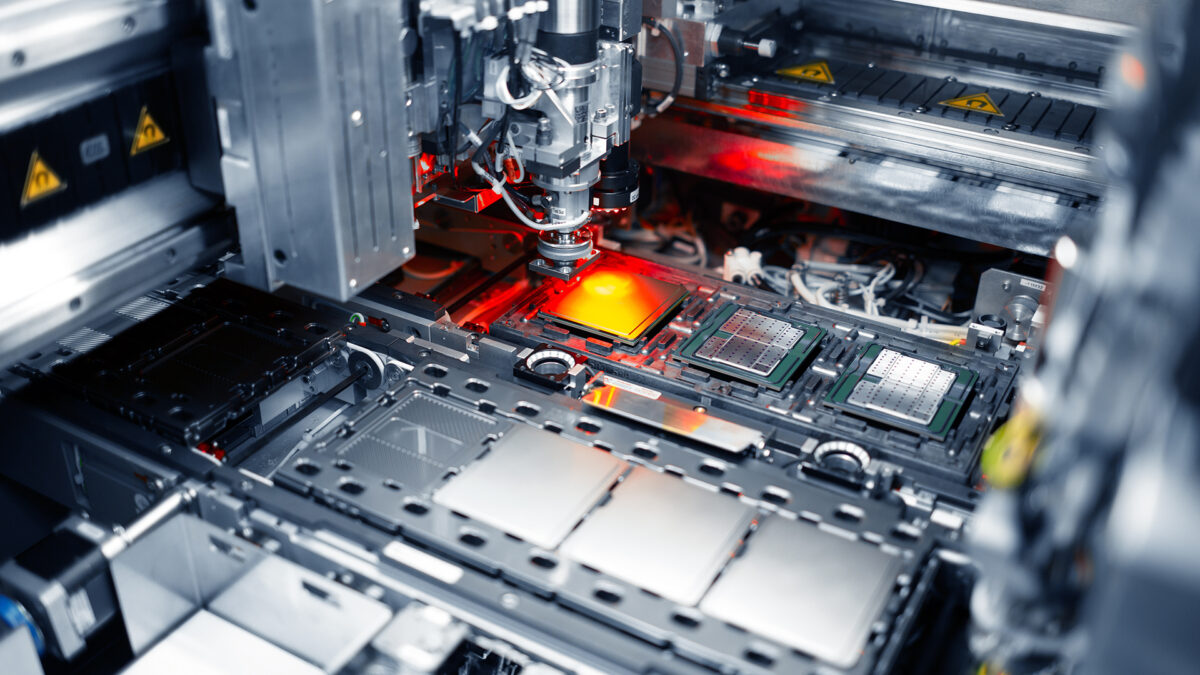 Close-up of a semiconductor manufacturing machine with mechanical components and electronic circuits. The equipment is illuminated with red and white lights, highlighting the intricate details of the machinery in an industrial setting.