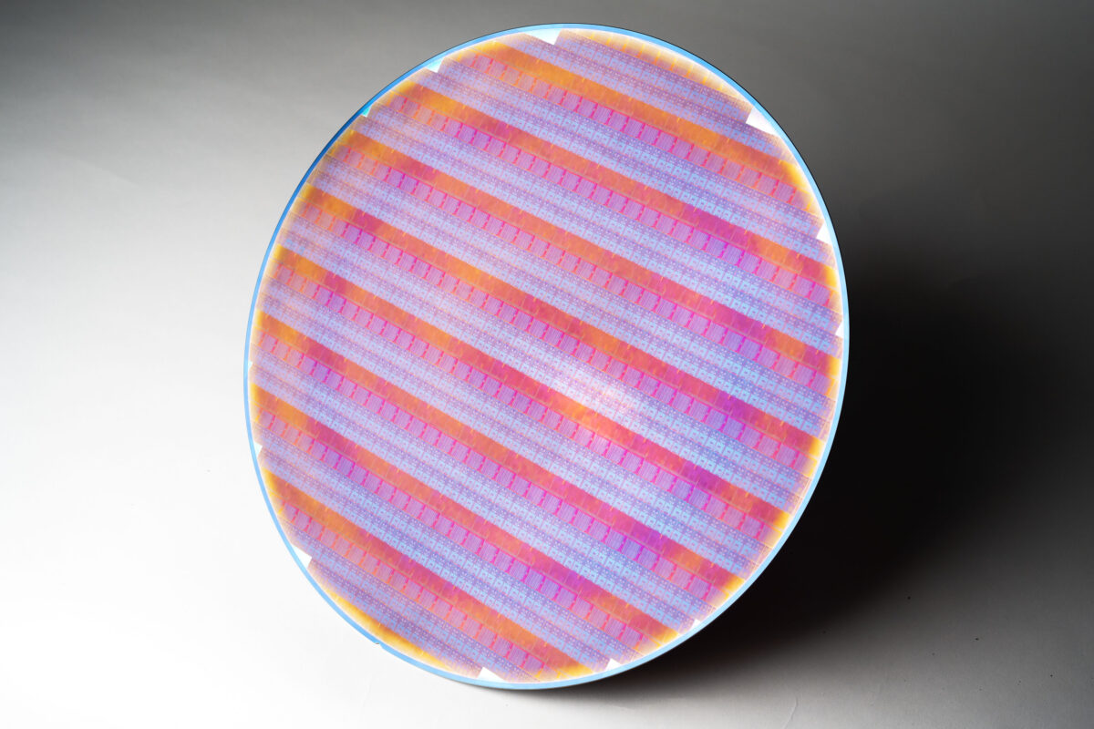 A circular plate with a vibrant pattern of diagonal pink, purple, and orange stripes, resembling a woven design. The plate is set against a plain gray background.