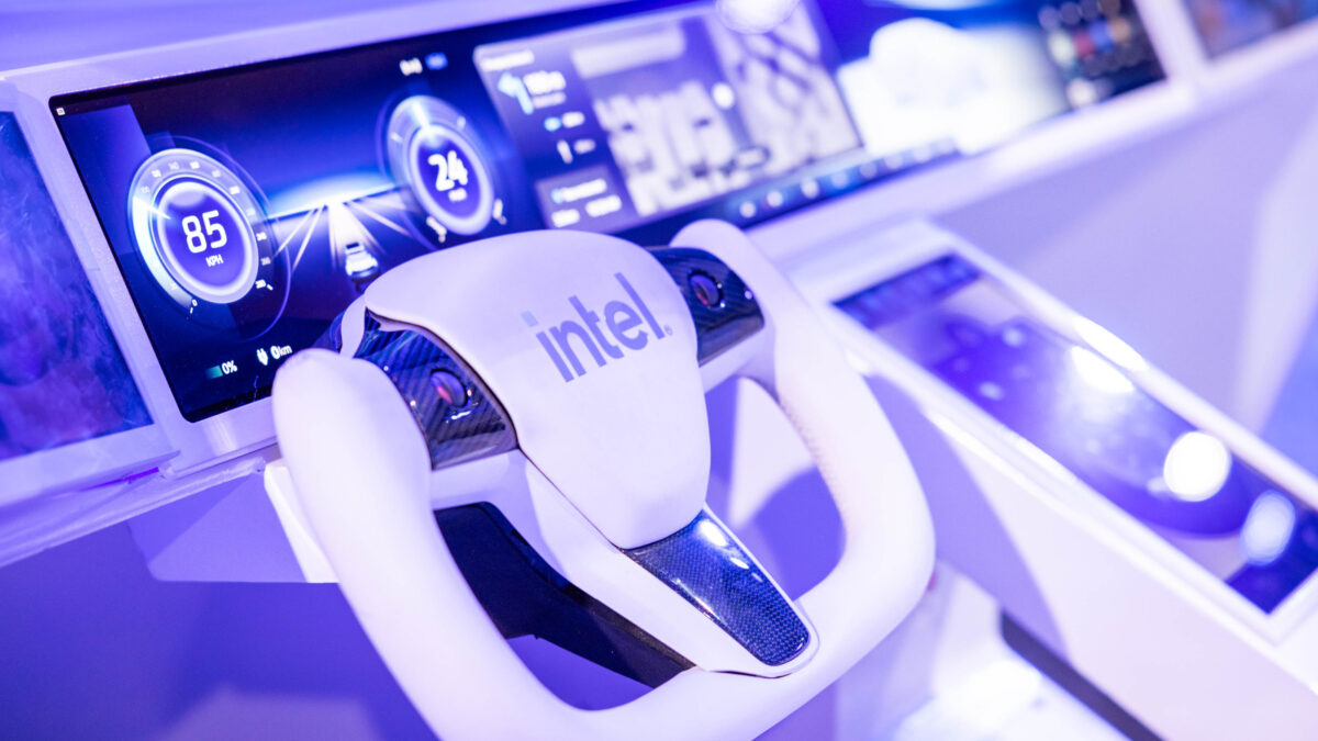 A modern car dashboard featuring a sleek, white steering wheel with Intel branding. Digital displays show speedometers and futuristic controls, illuminated in blue and white tones.