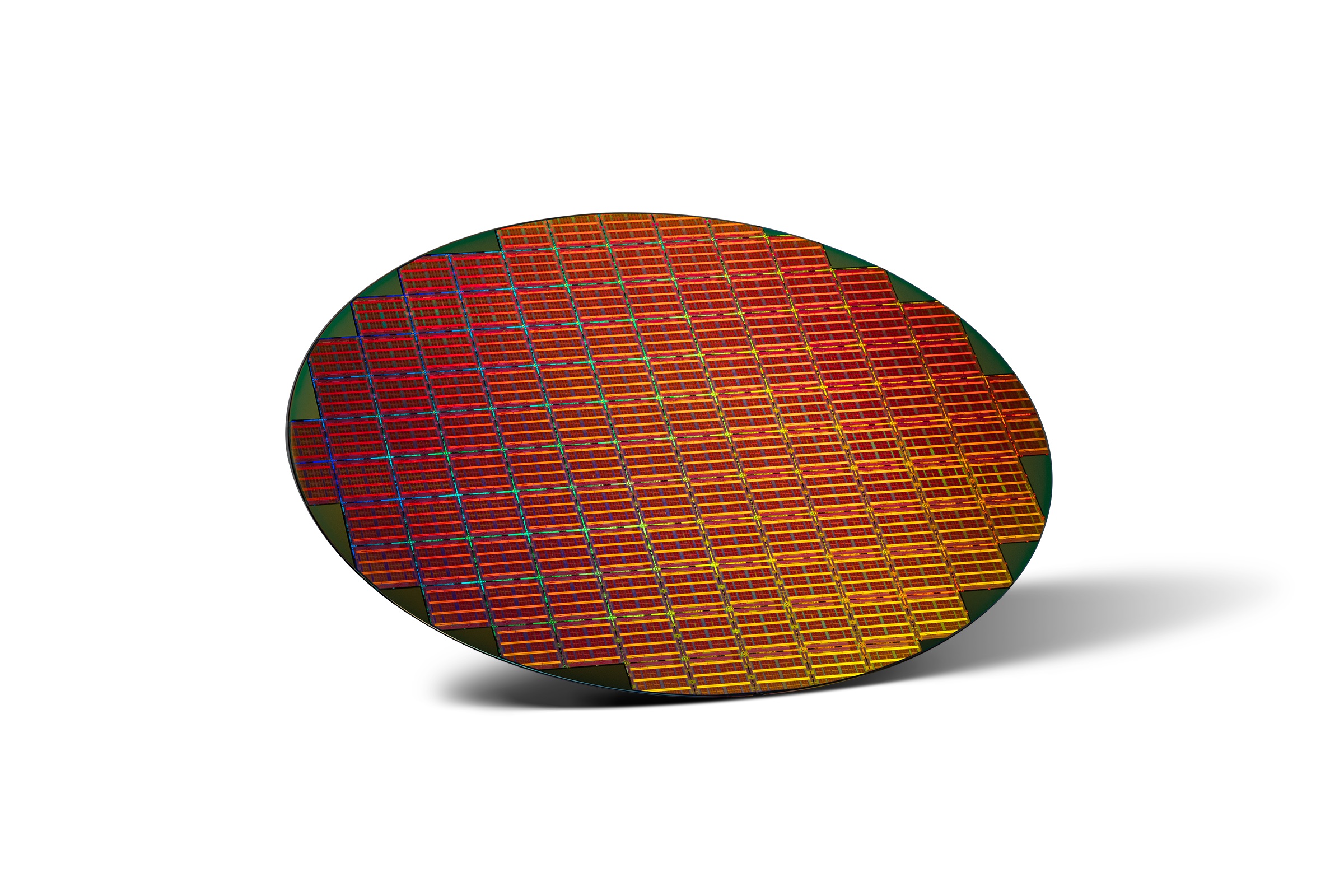 A circular silicon wafer with a grid of colorful microchips reflecting a spectrum of red, orange, and blue hues, placed against a white background with a subtle shadow on the right.