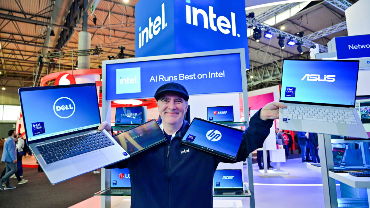 A person in an Intel cap holds four laptops from Dell, HP, and Asus, each displaying Intel logos on their screens. They are standing in front of an Intel booth with signage reading All Runs Best on Intel. Other tech brands are visible in the background.