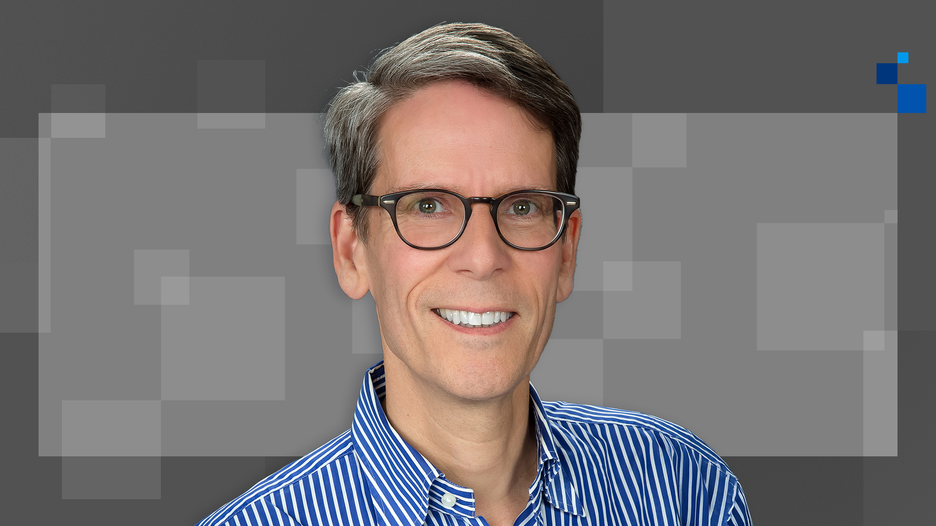 A person with glasses wearing a blue and white striped shirt smiles at the camera. The background features a blurred pattern of grey squares.