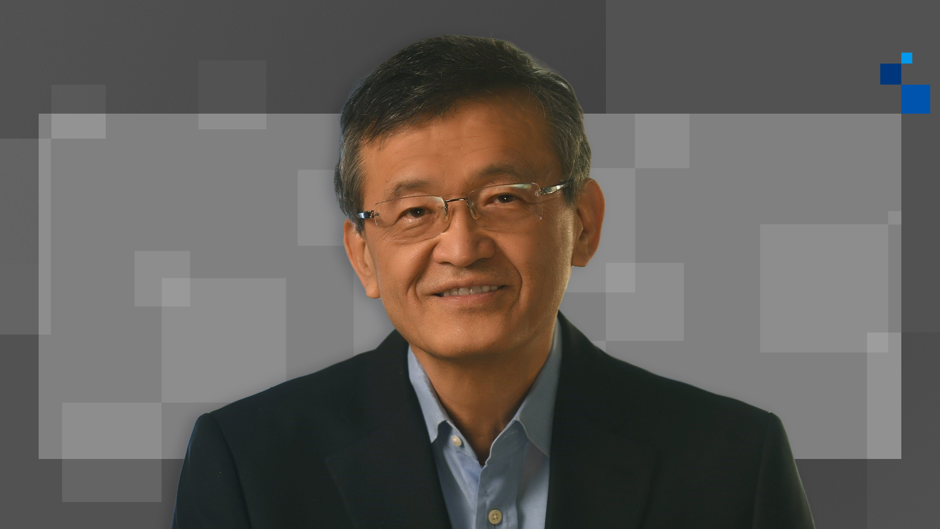 A man wearing glasses and a dark suit smiles at the camera against a geometric, pixelated gray and black background.